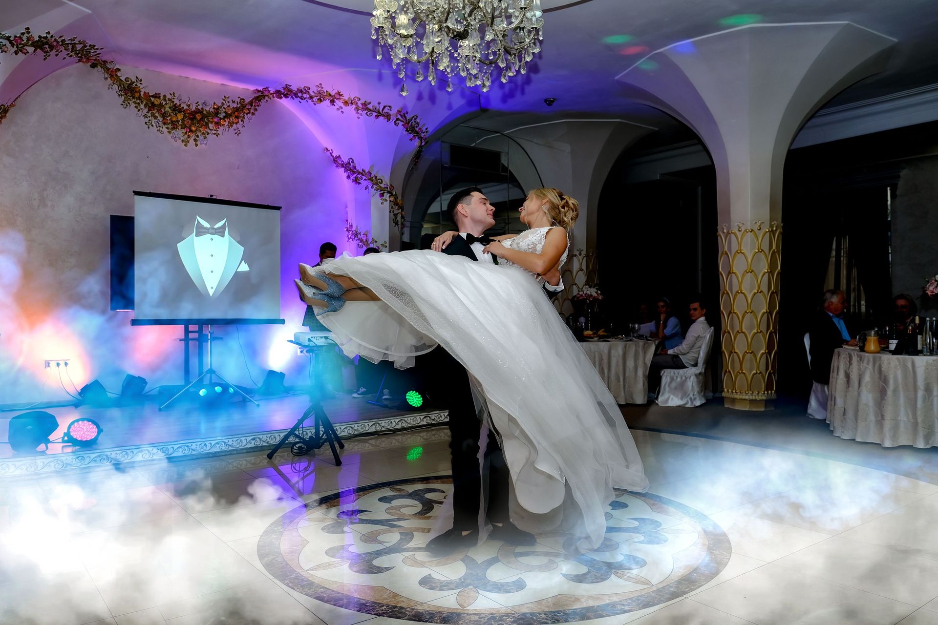 Bride and groom share an elegant dance at their wedding reception with vibrant lighting.